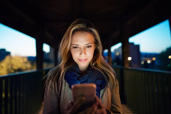 Женщина в городе по ночам держит смартфон, пишет смс . — стоковое фото