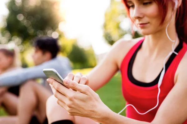 Junge Sportlerin im Park hält Smartphone in der Hand, hört Musik. — Stockfoto
