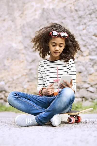Krásná africká americká dívka s smartphone a skateboard. — Stock fotografie