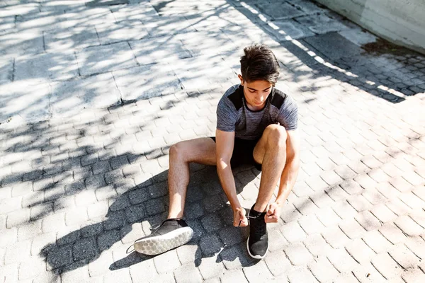 Běžec ve městě sedí na betonové cestičce vázání tkaničky. — Stock fotografie