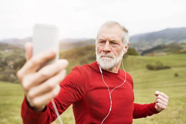 Corredor sênior ativo na natureza tomando selfie com telefone inteligente . — Fotografia de Stock