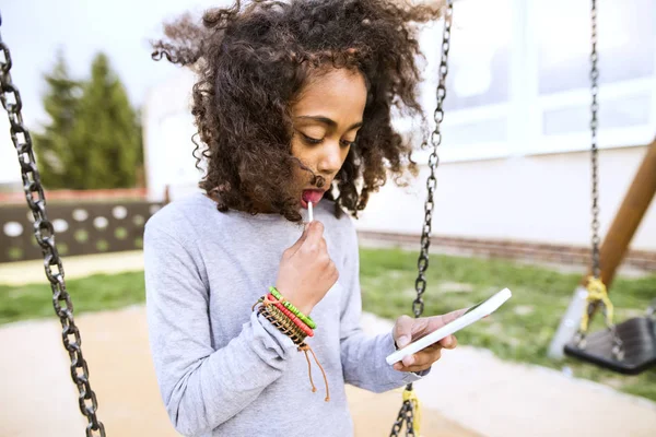 Africano menina americana no balanço com mensagens de texto telefone inteligente . — Fotografia de Stock