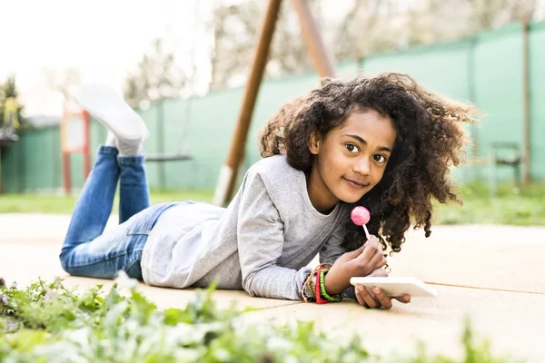 Bella ragazza afroamericana con smart phone, mangiare lecca-lecca — Foto Stock