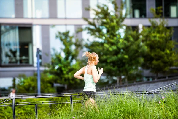 Hermosa joven atleta corriendo frente a edificios de vidrio . — Foto de Stock