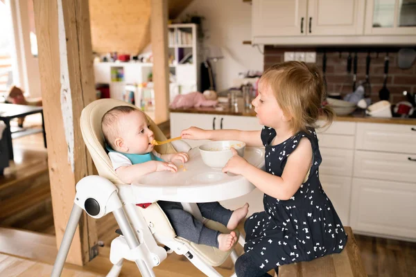 Menina bonito em casa alimentando seu irmão bebê . — Fotografia de Stock
