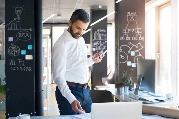 Empresário com smartphone e laptop em seu escritório . — Fotografia de Stock