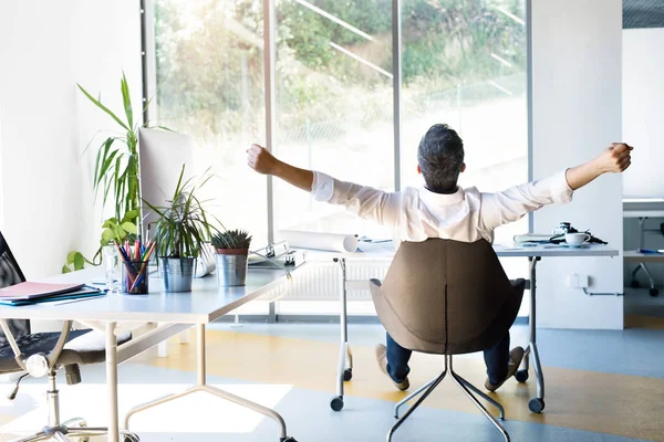 Empresário na mesa em seu escritório esticando os braços . — Fotografia de Stock