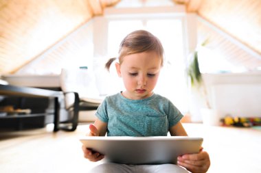 Küçük kız evde tablet bir şey izliyor.