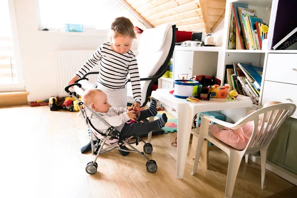 Niña en casa con hermano pequeño en cochecito de juguete . — Foto de Stock