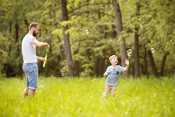 Hipster father and son blowing bubbles outdoors in park. — Stock Photo, Image