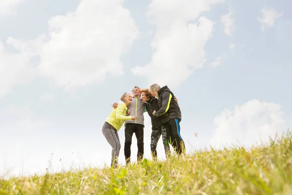 Grupo de corredores senior al aire libre, descansando, sosteniendo los brazos . — Foto de Stock