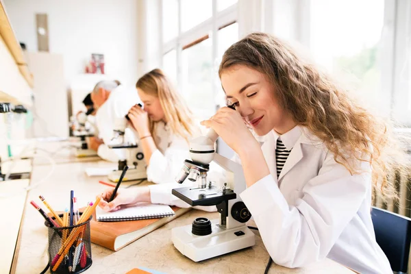 Belos alunos do ensino médio com microscópios em laboratório . — Fotografia de Stock