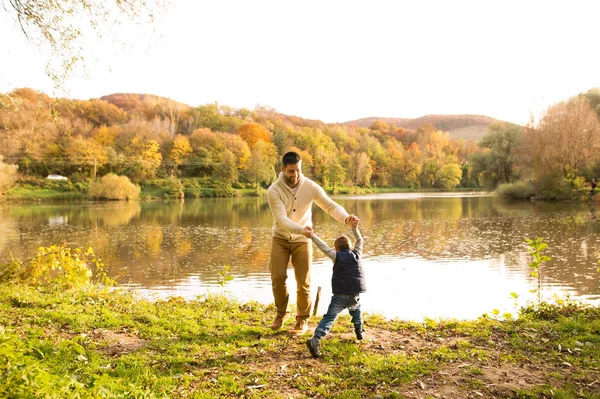 Vater hält seinen kleinen Sohn und dreht ihn. Herbstliche Natur. — Stockfoto