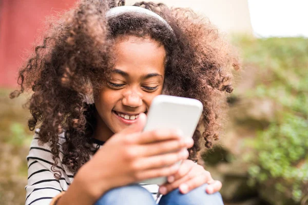 Menina americana africana bonita com telefone inteligente e fones de ouvido . — Fotografia de Stock