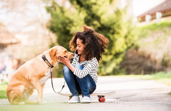 Africana americana chica al aire libre en monopatín con su perro . — Foto de Stock
