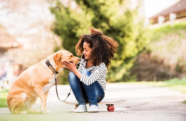 Africano americano menina ao ar livre no skate com seu cão . — Fotografia de Stock