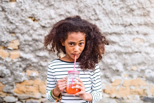 Bella ragazza africana americana che beve succo, vecchio wal di cemento — Foto Stock