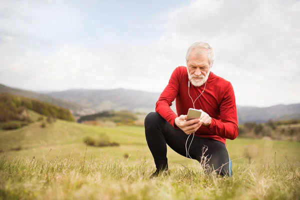 Aktivní senior běžec v přírodě s chytrý telefon a sluchátka. — Stock fotografie