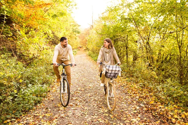 Young couple in warm clothes cycling in autumn park. — Stock Photo, Image