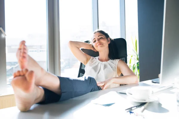 Affärskvinna i hennes kontor som sitter med benen på skrivbord. — Stockfoto