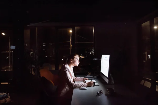 Businesswoman in front of computer screen in office at night.