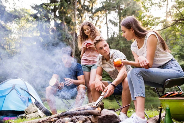 Tieners kamperen, koken van vlees op vreugdevuur. — Stockfoto