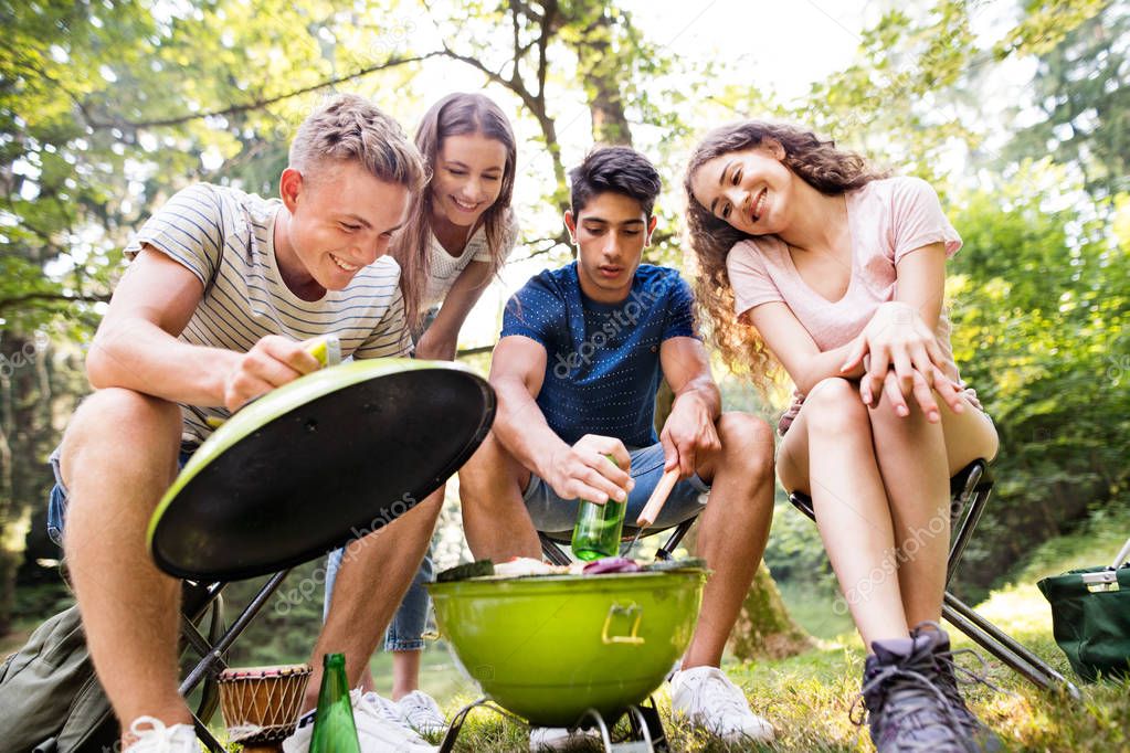Teenagers camping, cooking meat on barbecue grill.