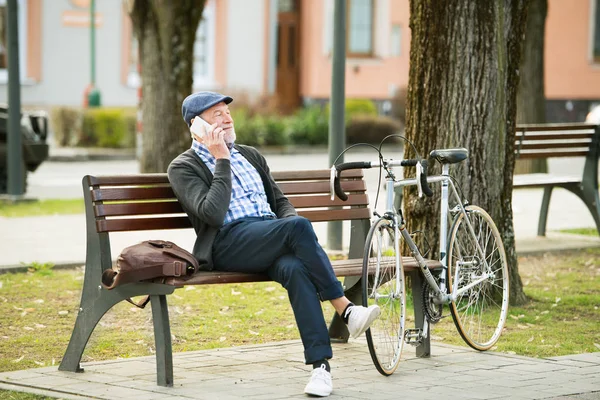 Hombre mayor con bicicleta y teléfono inteligente, haciendo una llamada telefónica —  Fotos de Stock