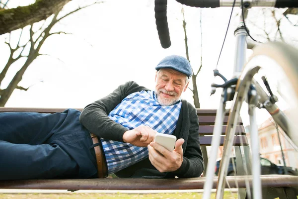 Homme âgé avec vélo en ville, tenant un téléphone intelligent, textos — Photo