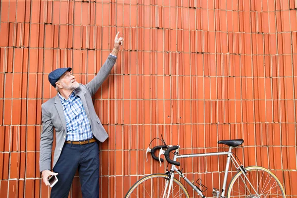Homem sênior com bicicleta de pé contra a parede de tijolo . — Fotografia de Stock