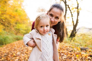 Anne ve kızı sonbahar ormandaki bir yolda.