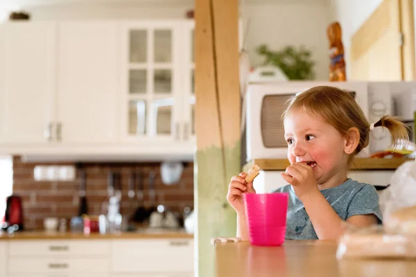 Liten flicka hemma äta ett mellanmål. — Stockfoto