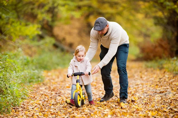 Far med lilla dotter cykling i höst park. — Stockfoto