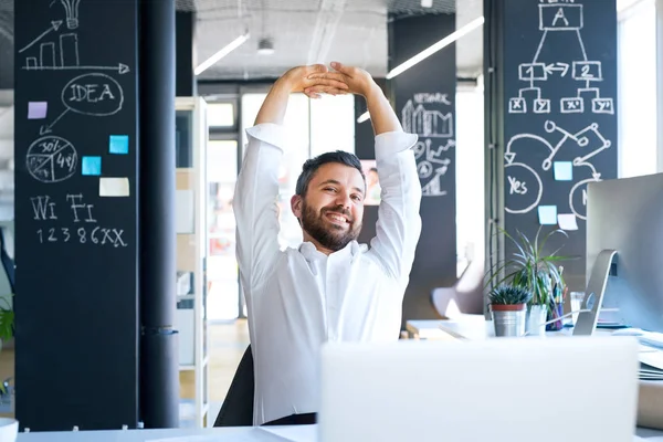 Empresario en el escritorio de su oficina estirando los brazos . — Foto de Stock