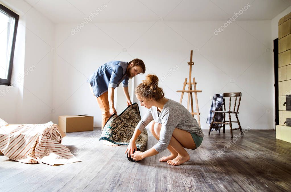 Young couple moving in new house, rolling out carpet.