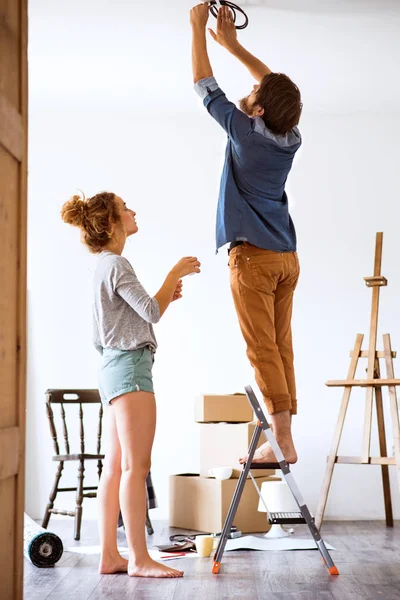 Casal jovem que se move na casa nova, mudando uma lâmpada . — Fotografia de Stock