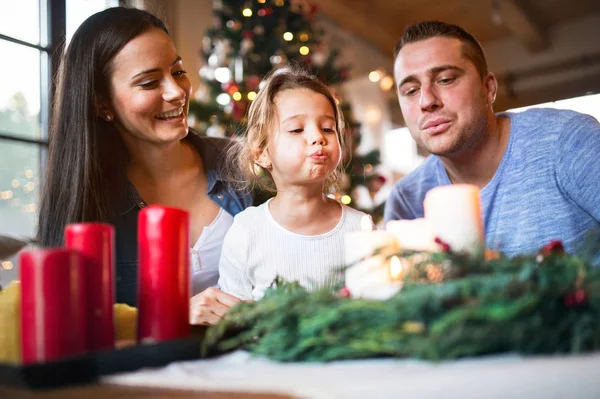 Mladá rodina foukání svíčky na adventní věnec. — Stock fotografie