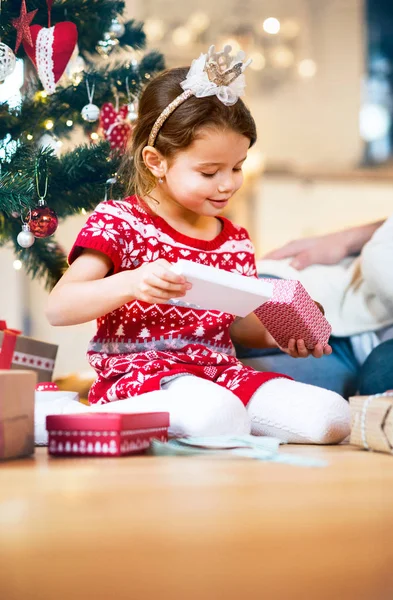 A karácsonyfa, ajándékok kicsomagolás alatt a kislány. — Stock Fotó