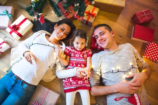 Young family lying under Christmas tree among presents, — Stock Photo, Image