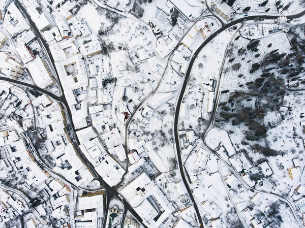 Aerial view of small town with many hills and forest surrounding it. Winter time.
