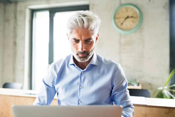 Rijpe zakenman met laptop in creatieve kantoor. — Stockfoto