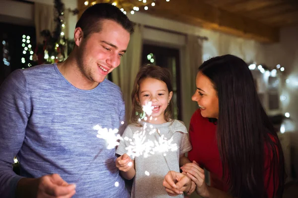 Young family with sparklers at Christmas time at home. — Stock Photo, Image