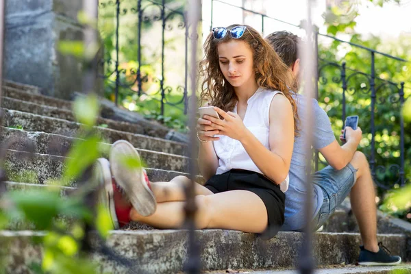 Jeune couple avec smartphones assis sur les escaliers en ville . — Photo