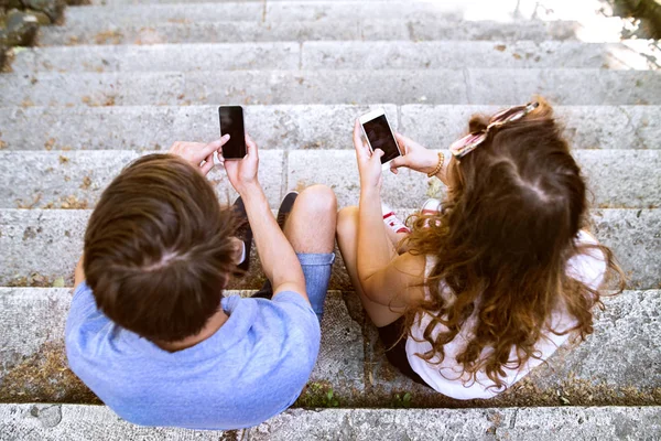 Jong (echt) paar met smartphones zittend op de trap. — Stockfoto