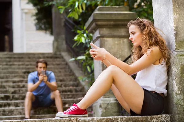 Молодая пара со смартфонами сидит на лестнице в городе . — стоковое фото