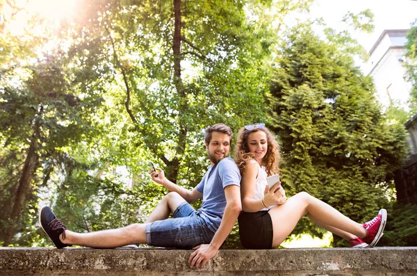 Jeune couple avec smartphones en ville assis sur un mur de béton . — Photo