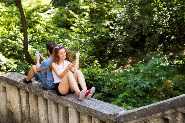 Pareja joven con smartphones en la ciudad sentada en una pared de hormigón . — Foto de Stock