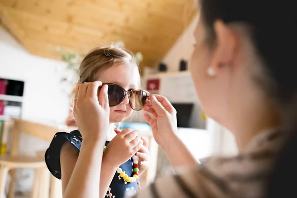 Mother puts on sunglasses to her cute little daughter. — Stock Photo, Image