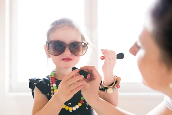 Madre pintando labios de su linda hijita con lápiz labial . — Foto de Stock