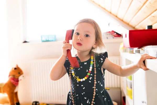 Cute little girl in dress wearing red lipstick making phone call — Stock Photo, Image